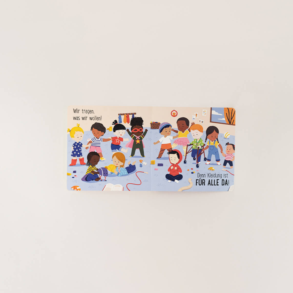Auf einer Kinderbuch-Seite des Zuckersüß Verlag-Titels "Spielzeug ist für alle da & Kleidung ist für alle da" spielen, zeichnen und verkleiden sich Kinder bunt. Der deutsche Text: "Wir tragen, was wir wollen! Kleidung ist FÜR ALLE DA!.